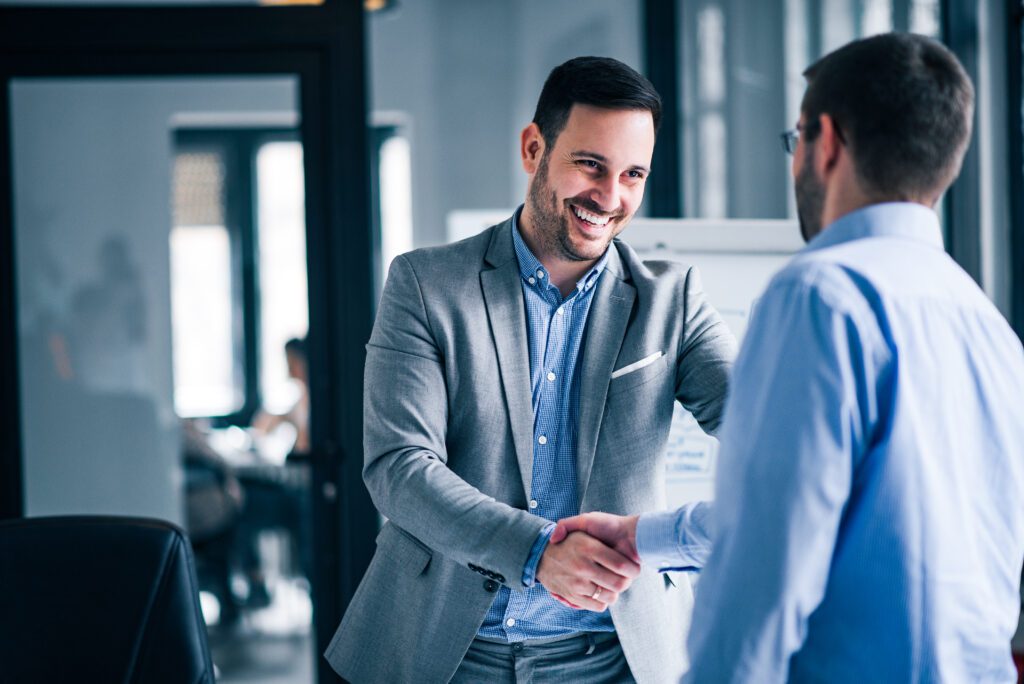 Two smiling businessmen shaking hands while standing in an offic